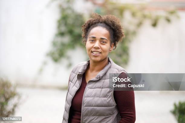 Coiled Hair Woman Smiling And Wearing A Padded Vest Stock Photo - Download Image Now