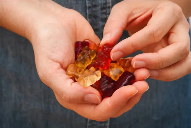 Woman hand taking a Gummy bear candy from her palm full of Gummy bears candies