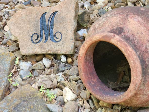decorative flower pot and initial m in rock filled flower bed. - letter m alphabet color image flower imagens e fotografias de stock