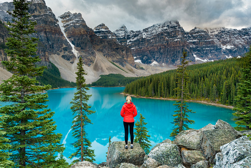 Female hiker in red jacket stood looking over Lake Moraine in Banff National Park, Alberta, Canada