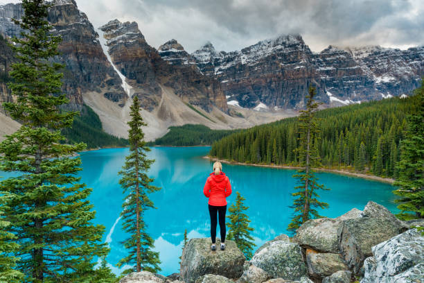 female hiker stood looking over lake moraine, banff national park, canada - alberta mountain lake landscape imagens e fotografias de stock