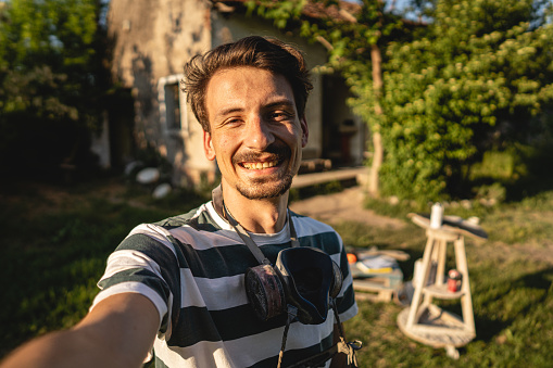 Portrait of Caucasian male craftperson taking selfie at his outdoor workshop