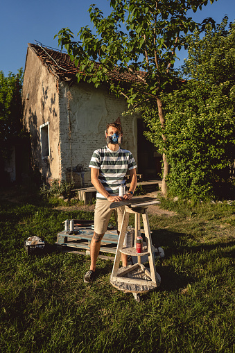 Male Caucasian artist, spray painting the skateboard at his outdoor workshop