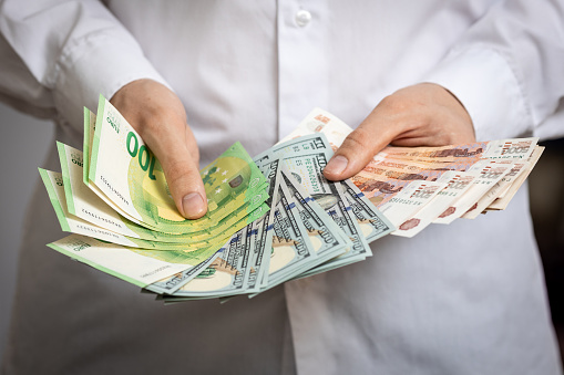Cash rubles, dollars and euros close-up in the hands of a man in a white shirt.