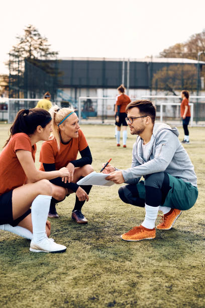 istock Young coach and female soccer players analyzing  game plan on playing field. 1397755902