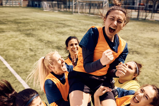 We won the game! Cheerful team of female soccer players celebrating victory and carrying on of teammates who is shouting out of joy on stadium. soccer team stock pictures, royalty-free photos & images