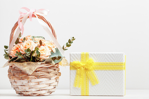 Fresh pink flowers in a basket and a box with a gift on the table with copy space.