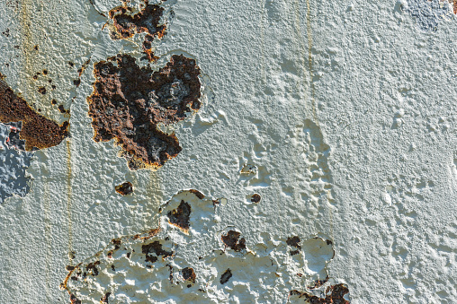 Rusty metal surface with cracked white paint in the sun.