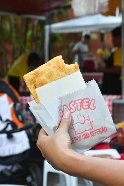 pastel fried empanada, a hand holding it, in the fair during the day