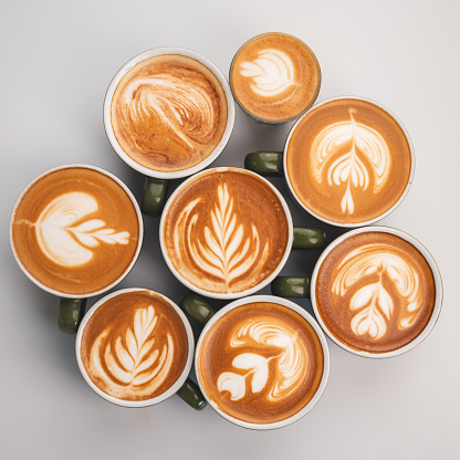 Closeup of hands of a young male barista creating pattern and design using cream and utensil on freshly brewed and made cappacino coffee and frappe in cafeteria for customer