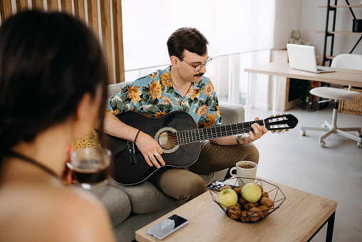 Shot of a young man playing the guitar while his wife has a cup of coffee at home