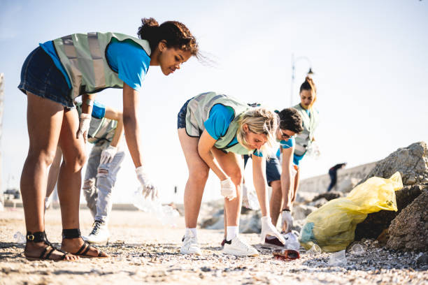 des gens divers nettoient la plage, des bénévoles ramassent les déchets sur la côte, des jeunes travaillant en équipe conscients de la pollution produite par l’industrie du plastique - dépollution photos et images de collection