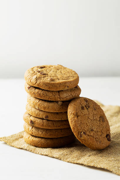 istock chocolate chip cookies. stack of biscuits on the sackcloth with copy space on white background. Chocolate cookies on white linen napkin on wooden table. vertical 1397776883
