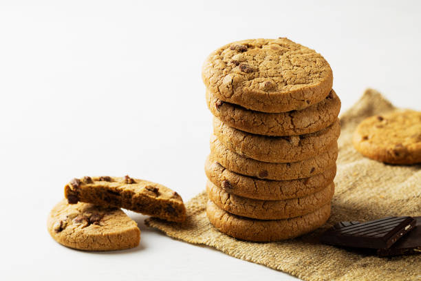 biscotti con gocce di cioccolato su sfondo bianco.pila di biscotti con pezzi di cioccolato sul sacco con spazio di copia su sfondo bianco. biscotti al cioccolato su tovagliolo di lino bianco su tavolo di legno. - oat oatmeal isolated stack foto e immagini stock