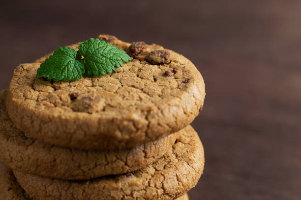 primi piani biscotti con gocce di cioccolato. biscotti al cioccolato con foglie verdi di menta sul tavolo di legno. pila di biscotti con pezzi di cioccolato su sacco con spazio di copia su sfondo scuro. - oat oatmeal isolated stack foto e immagini stock