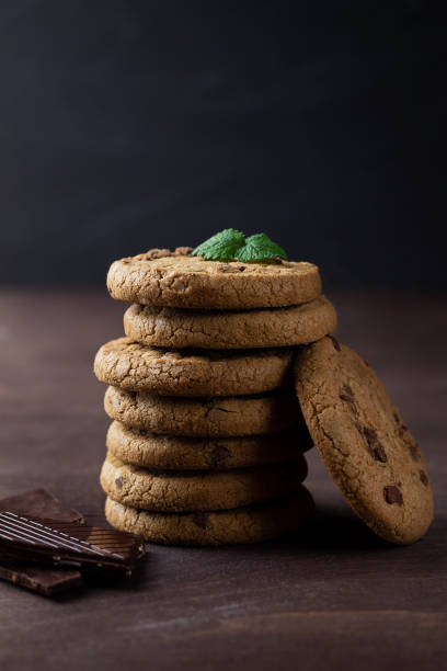 biscotti con gocce di cioccolato sul tavolo di legno. biscotti al cioccolato con foglie verdi di menta sul tavolo di legno. pila di biscotti con pezzi di cioccolato con spazio copia su sfondo scuro. verticale - oat oatmeal isolated stack foto e immagini stock