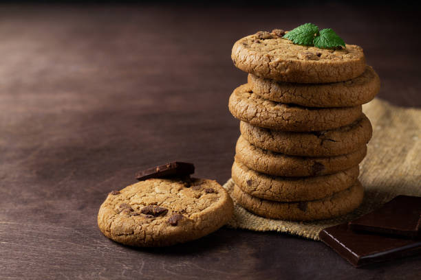 biscotti con gocce di cioccolato. biscotti al cioccolato con foglie verdi di menta sul tavolo di legno. pila di biscotti con pezzi di cioccolato su sacco con spazio di copia su sfondo scuro. - oat oatmeal isolated stack foto e immagini stock