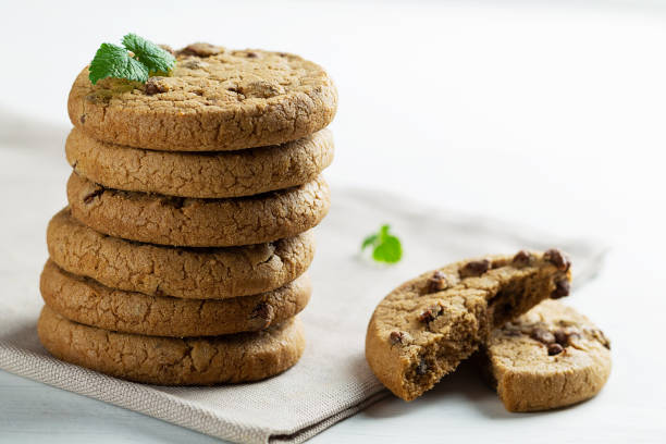 biscotti con gocce di cioccolato con foglie verdi di menta.pila di biscotti con pezzi di cioccolato con spazio di copia su sfondo bianco. biscotti al cioccolato su tovagliolo di lino bianco su tavolo di legno. - oat oatmeal isolated stack foto e immagini stock