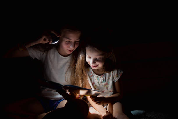 istock two sisters reading a book at night with a flashlight 1397777561
