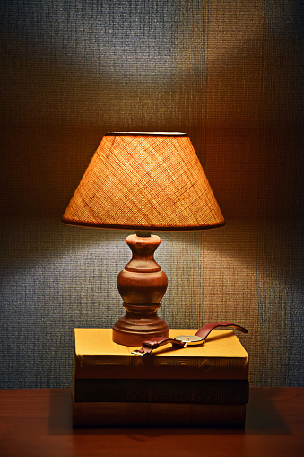 Reading lamp, books and watches. Soft light of Desk Lamp. Evening time. Interior of Cabinet, room. Copy space. Vertical photo. Selective focus.