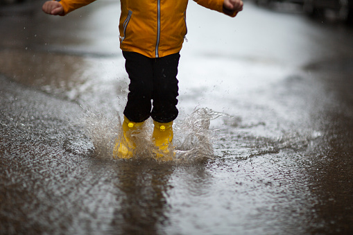 Legs of child in yellow rubber boots jumping in puddles