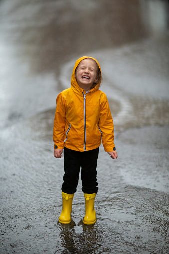 Legs of child in yellow rubber boots jumping in puddles