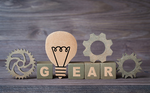 Word GEAR made from letter blocks with cogs and a wooden lightbulb shape on a wooden background. Business idea development concept.