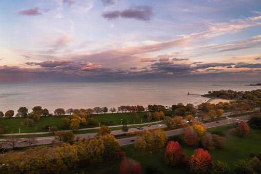 A beautiful autumn sunset over Lake Michigan and Lake Shore Drive in Chicago with pink and blue clouds and red, yellow and green fall foliage.