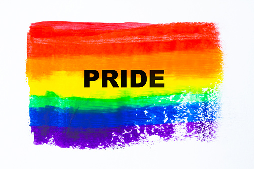 Pride written on a painted rainbow flag.\nLGBTQIA concept image. Love is love.