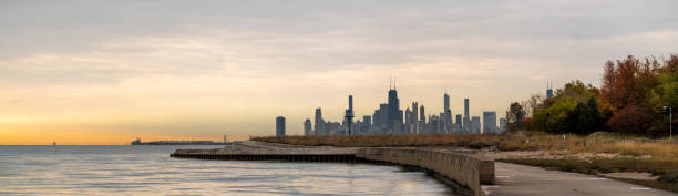 A panorama of the Chicago Skyline at sunrise with orange clouds in the sky and water below in autumn with colorful tree foliage. stock photo