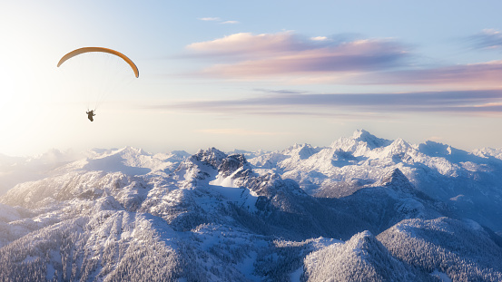 Adventure Composite Image of Paraglider Flying up high in the Rocky Mountains. Sunny Sunset Sky. Aerial Background from British Columbia, Canada. Extreme Sport Concept. Panorama. winter