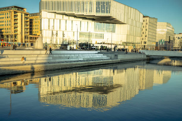 Oslo, Norway - March 12, 2022: Relax in the calm winter afternoon in Fjord City of Oslo. People are sitting on the steps of the promenade, the others take a sauna and a bath in the freezing sea.