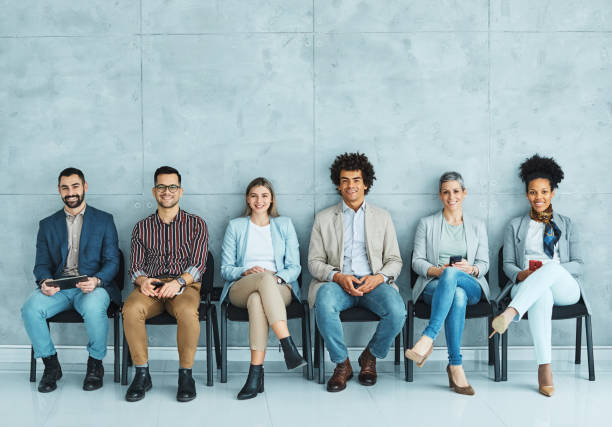 man business chair sitting waiting woman businessman candidate recruitment businesswoman office businessperson job young interview line Group of young business people sitting in chairs and waiting for an interview job search stock pictures, royalty-free photos & images