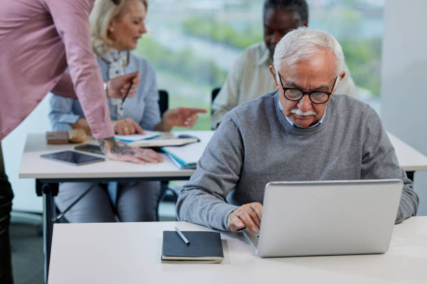 istock A senior man types on laptop in classroom while young teacher showing other students how to solve a school problem. 1397784110