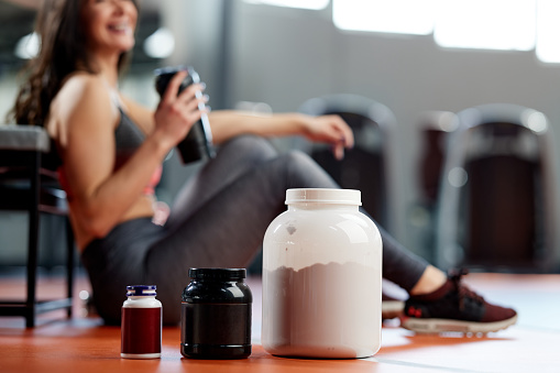 Selective focus on supplements and protein power in gym with a sportswoman.