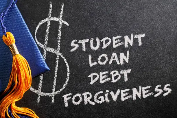 "Student Loan Debt Forgiveness" written on a chalk board as a graduation cap and a gold tassel rest on top.