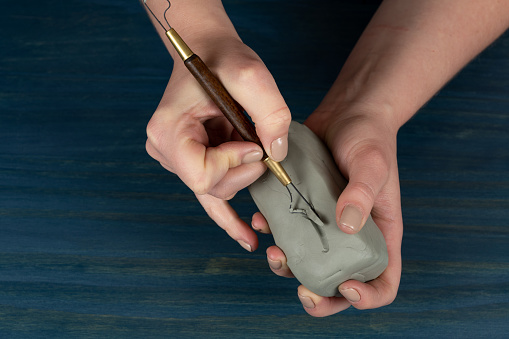 Closeup of an artist's hands carving clay with a tool on wooden blue table background