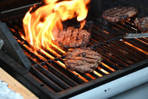 istock Four beef burgers being cooked on a gas fired barbecue with one burger surrounded with flames for a flamed grill burger as it is being flipped with a spatula 1397789165