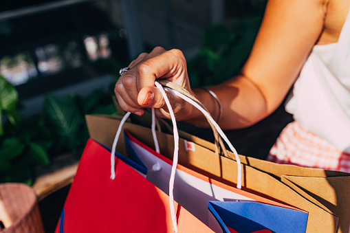 A cropped photo of an anonymous female Asian shopaholic holding shopping bags after buying some things at a shopping mall.