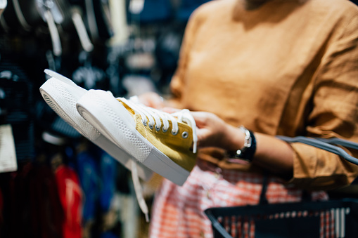 A close up shot of an anonymous female Asian shopaholic holding some yellow sneakers at a store and deciding whether to buy it or not.