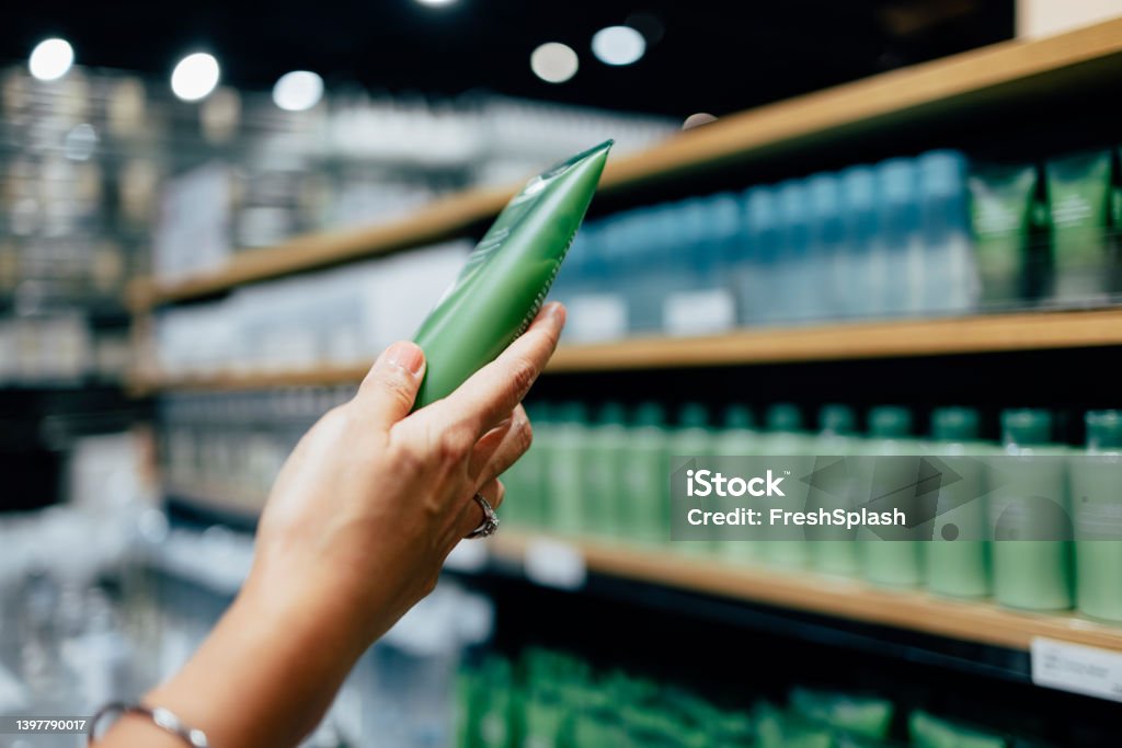 A Close Up View Of An Unrecognizable Female's Hand Holding Some Beauty Product A cropped photo of an anonymous Caucasian woman holding a tube of a hand cream while shopping at a store. Merchandise Stock Photo