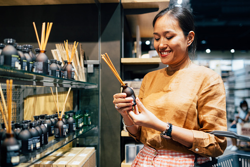 A smiling Asian female buying air freshener sticks at a store.