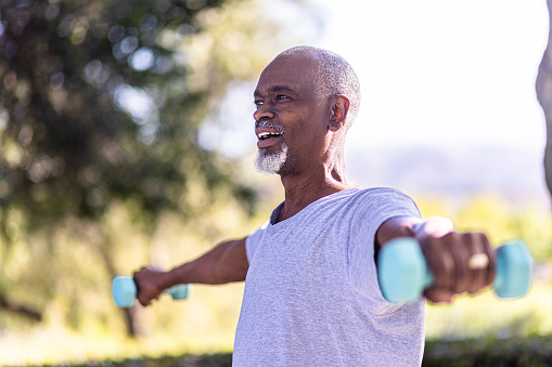 A senior black man working out outside with small weights
