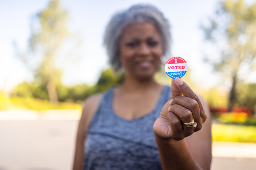 An older black woman holding an I voted sticker