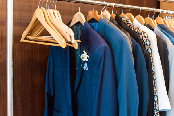 Several suit jackets hanging on hangers. Several suit jackets hanging on hangers. The first jacket has a flower on the lapel. Concept of dress suit for groom on his wedding day. businesswear stock pictures, royalty-free photos & images