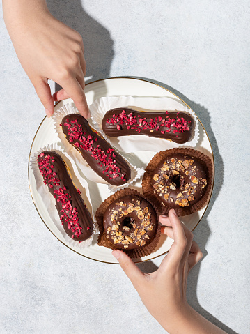 Hands holding eclairs and donut dessert . Assorted desserts. Sweet concept,