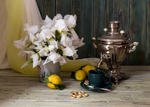 Rustic still-life with a samovar, a cup of tea and spring irises on a wooden table close-up