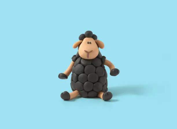 Photo of Cute sitting black sheep made of plasticine on blue background, Clay black sheep, outstanding, different, competitive, rebel. 3d artwork