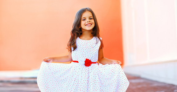 Portrait of happy smiling little girl child wearing white dress on city street