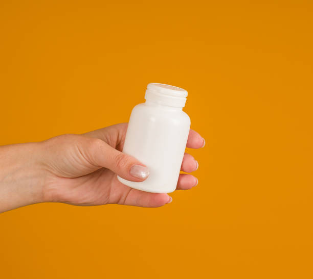 istock hand holds white bottle for pills on yellow background, close-up 1397798824